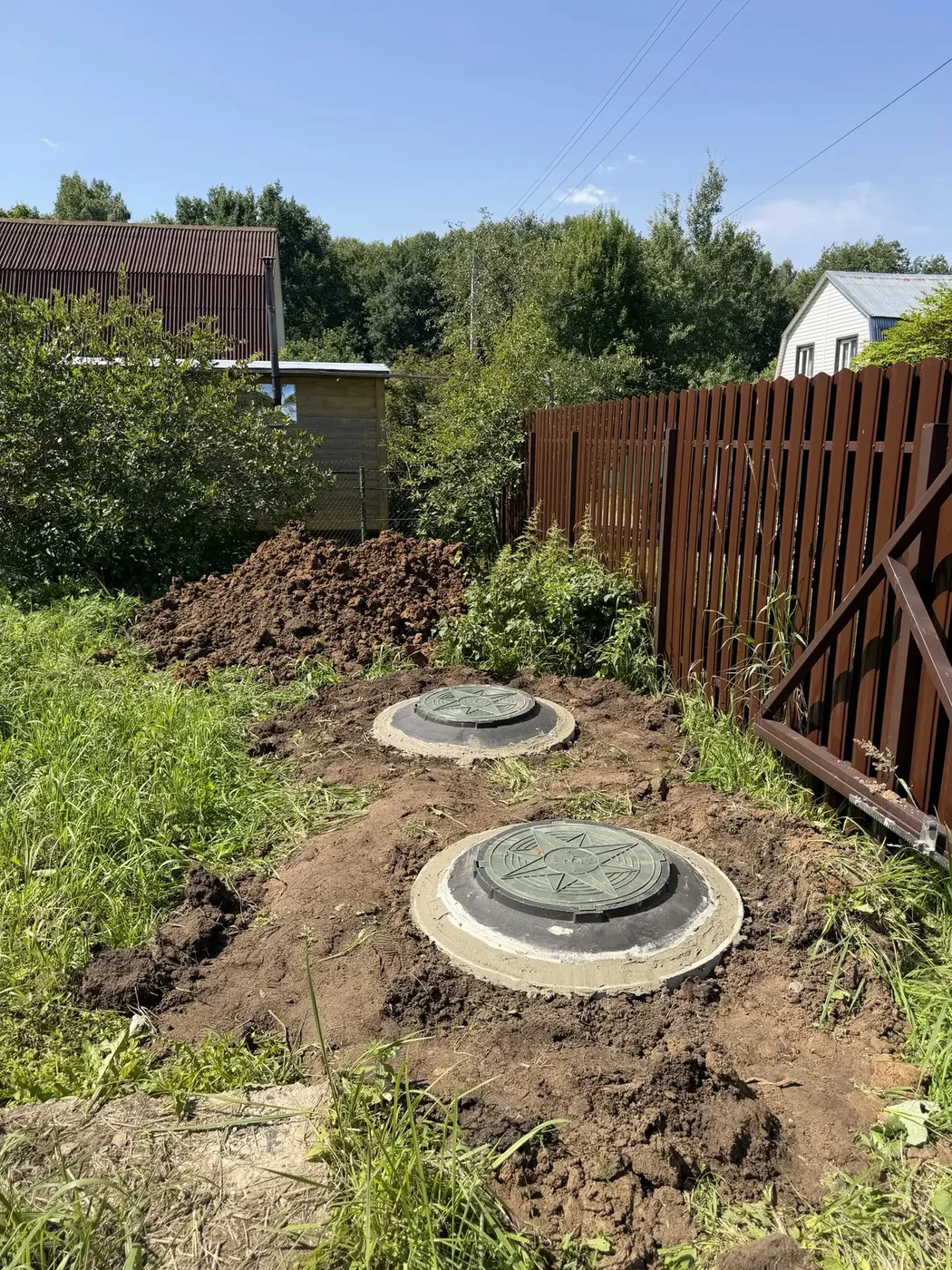 Два люка септика из колец у деревянного забора